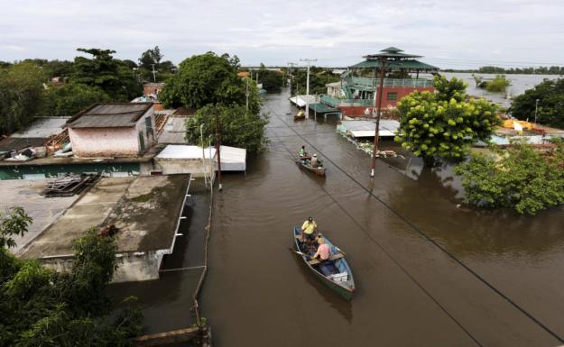 Men travel on a boat near flood-affected houses in Asuncion, December 27, 2015. More than 100,000 people have had to evacuate from their homes in the bordering areas of Paraguay, Uruguay, Brazil and Argentina due to severe flooding in the wake of heavy summer rains brought on by El Niño, authorities said on Saturday. REUTERS/Jorge Adorno